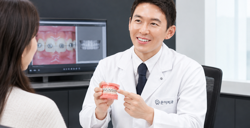 의료진이 교정 장치를 부착한 치아 모형을 가리키며 환자에게 치료 방법을 설명하는 모습